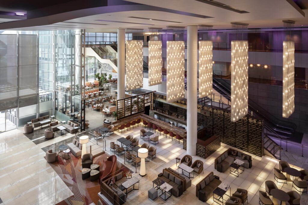 Spacious lobby atrium of the JW Marriott Los Angeles L.A. LIVE featuring elegant modern seating areas, large hanging light fixtures, a central bar, and floor-to-ceiling windows letting in natural light.