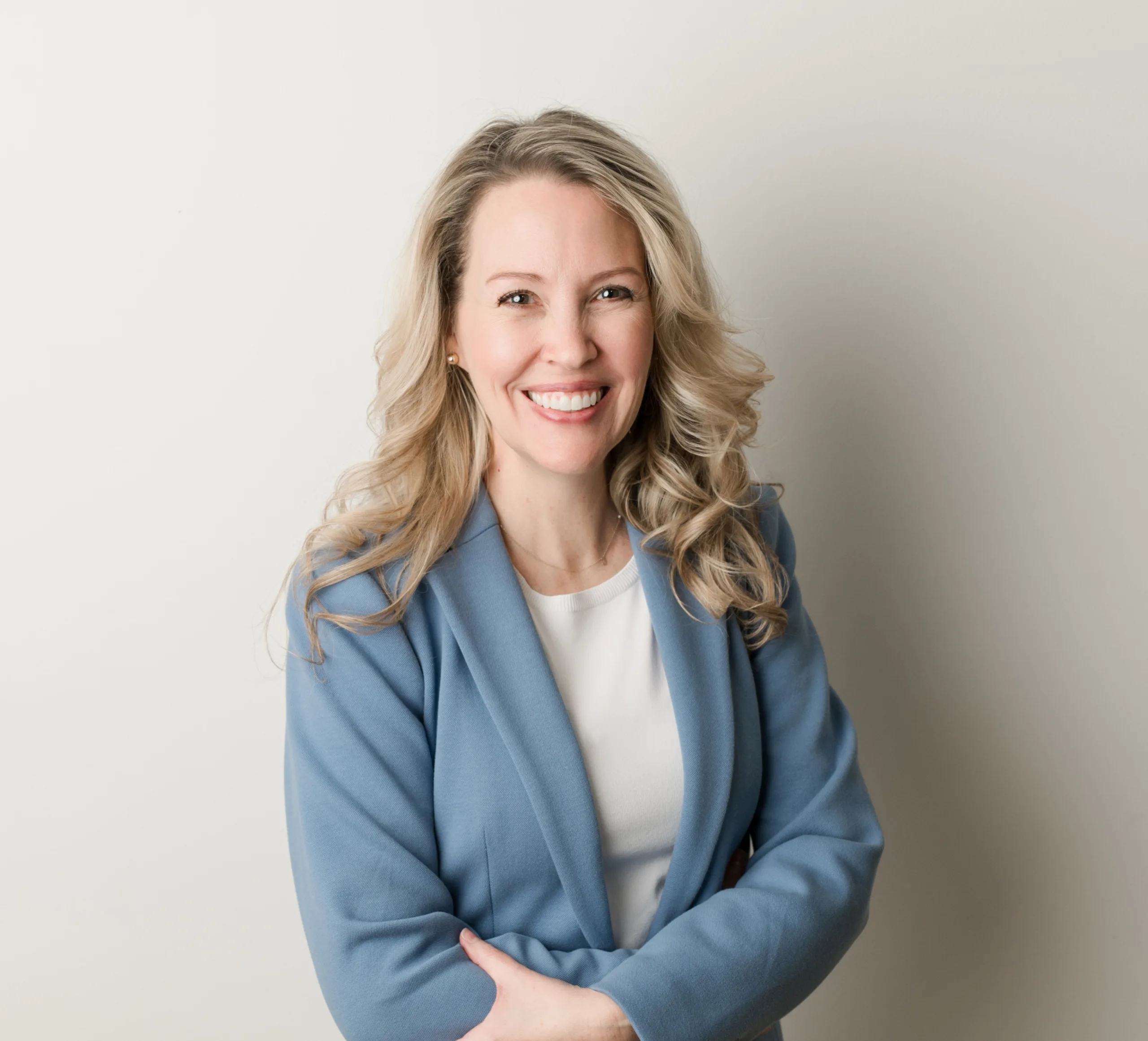 Smiling Shannon Avery with long blonde hair, wearing a light blue blazer and white top, posed against a neutral light background.